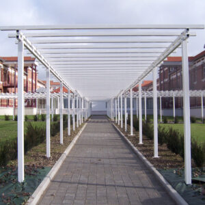 Pergola métallique blanche longeant une allée pavée dans un espace paysager.