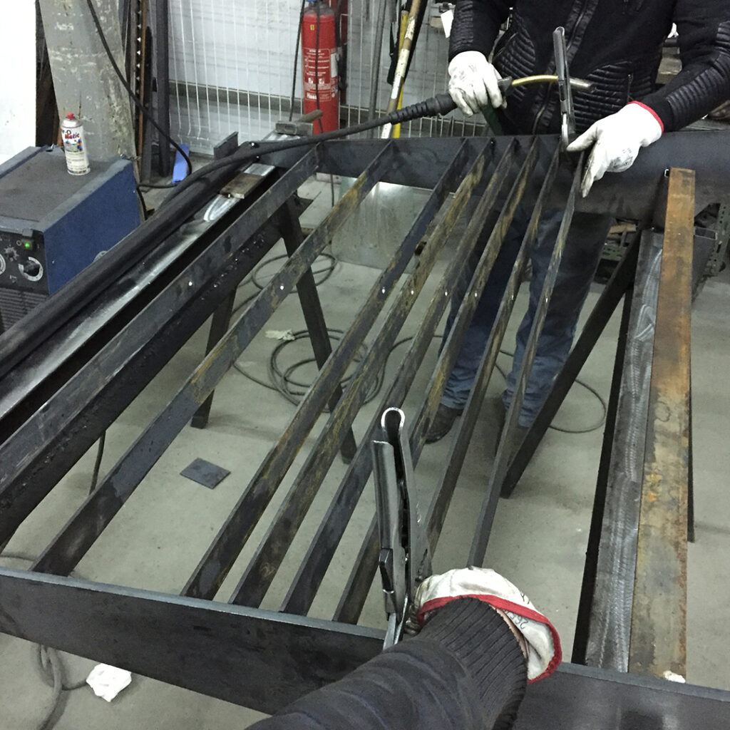 Opération de soudure dans un atelier de métallerie, en cours de fabrication d’un élément en acier avec structure à lames et serre-joints.