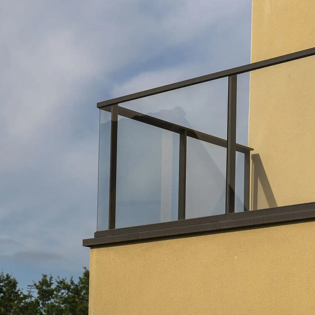Balustrade en verre sécurit avec structure métallique sombre, installée en façade d’un bâtiment contemporain pour sécuriser un balcon.