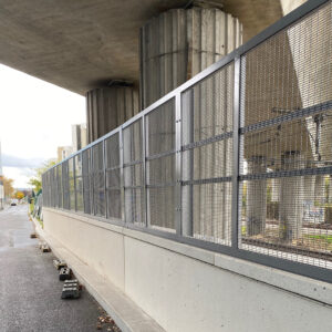 Clôture en acier avec tôle perforée installé sous un pont urbain.