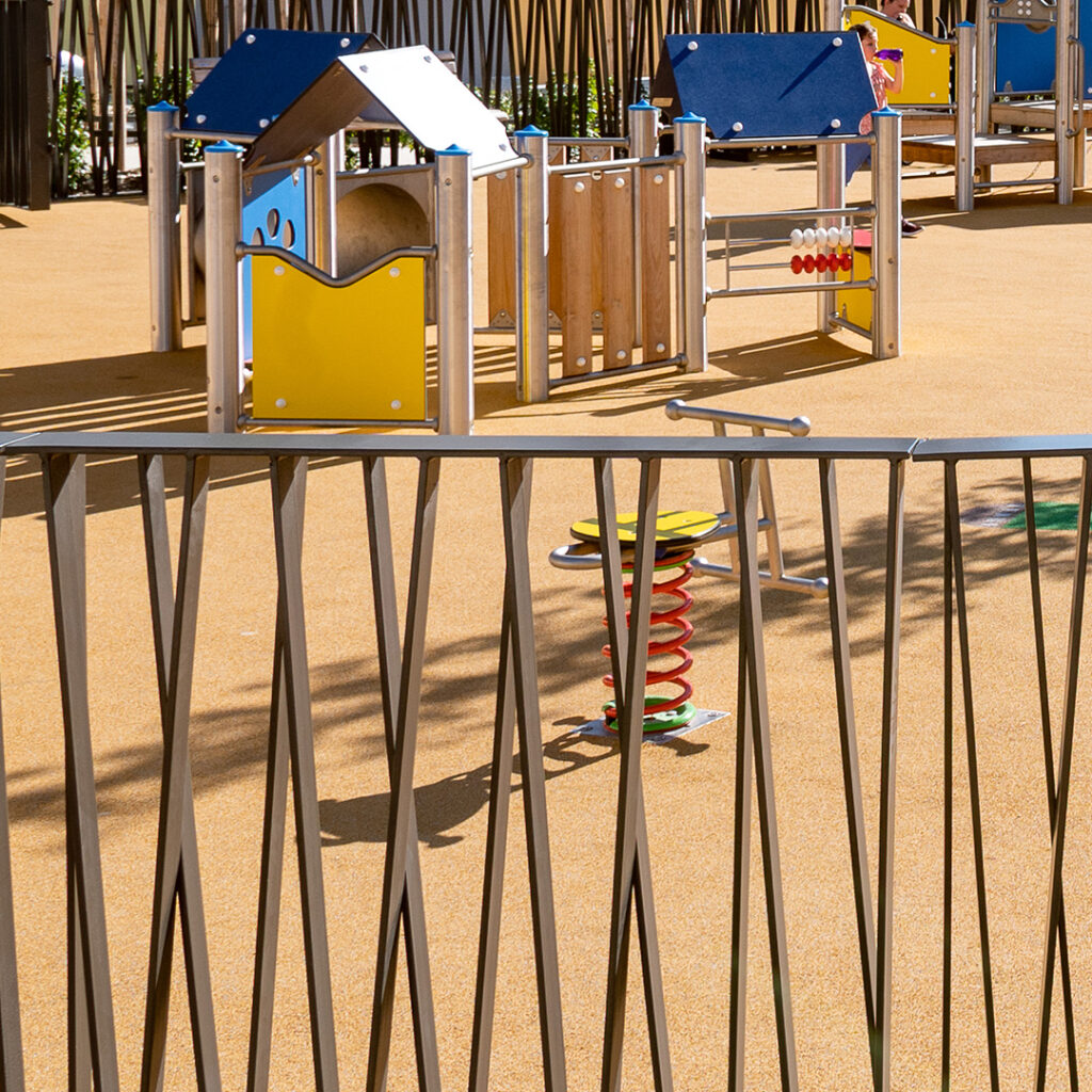 Clôture design en métal entourant une aire de jeux pour enfants, avec barreaudage oblique et décoratif.