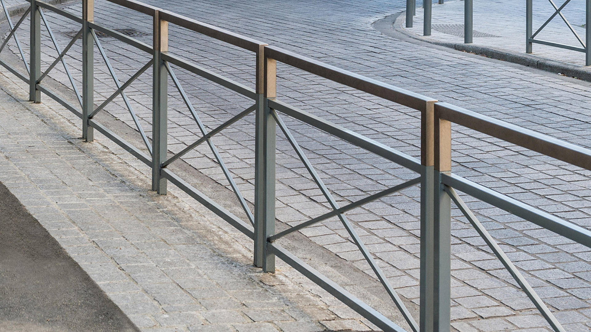 Barrière urbaine en acier avec lisse haute en bois, installée en bordure de voirie pavée pour sécuriser les circulations piétonnes.