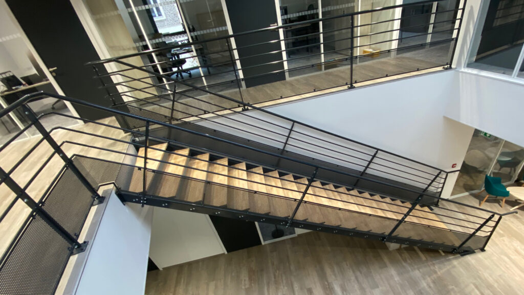 Escalier intérieur droit avec marches bois et structure métallique noire, équipé de garde-corps ajourés.