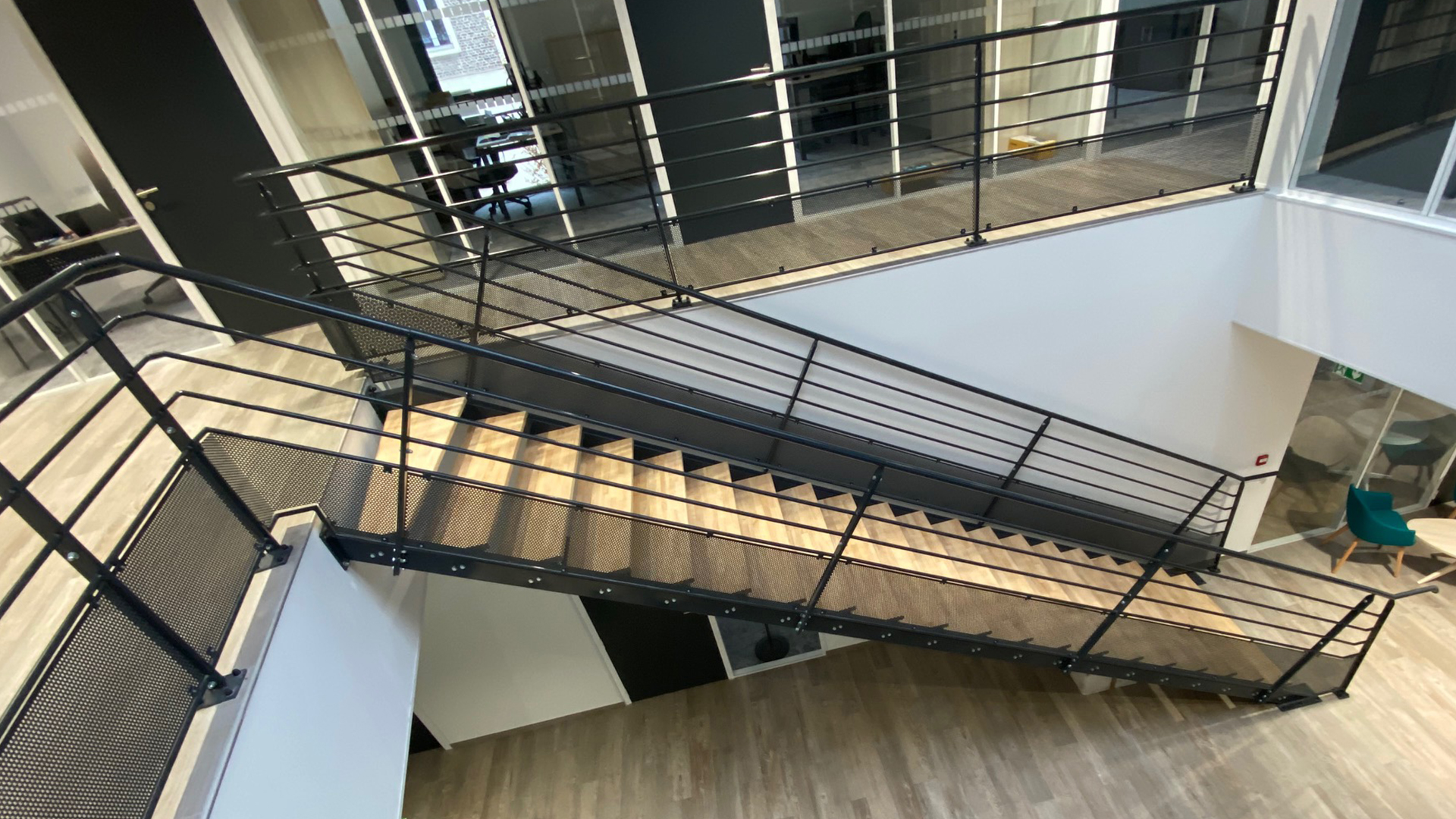 Escalier intérieur droit avec marches bois et structure métallique noire, équipé de garde-corps ajourés.