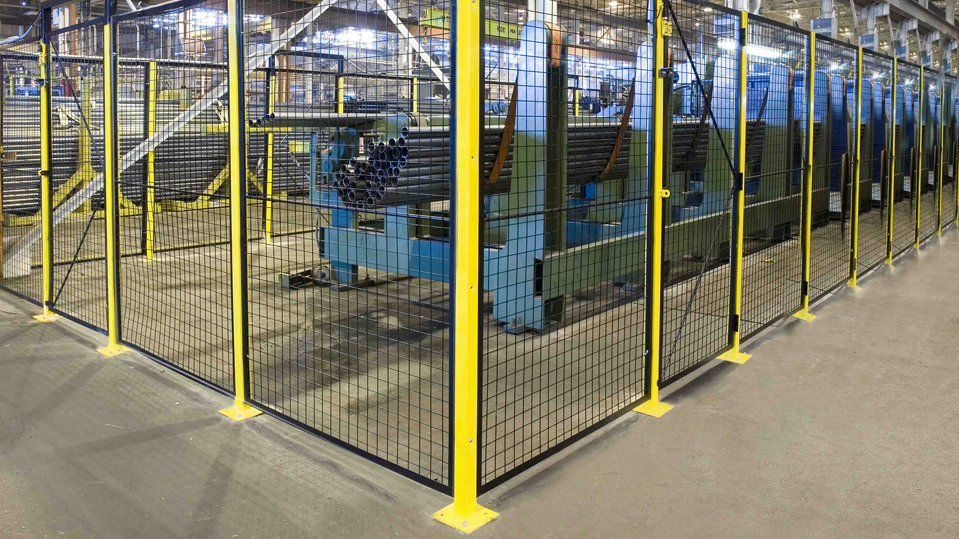 Clôture grillagée de sécurité avec poteaux jaunes, installée en usine pour protéger l’accès à une ligne de production ou une zone machine.