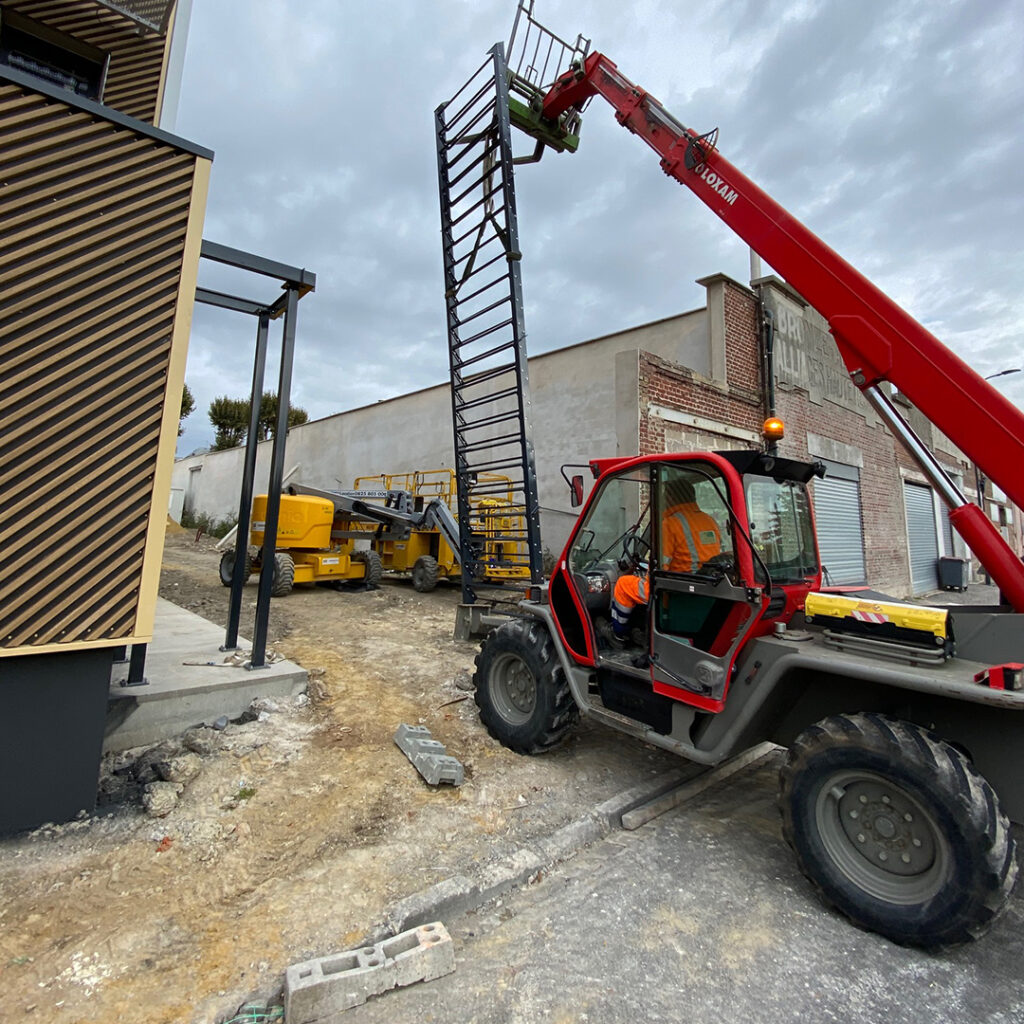Manutention d’un escalier métallique sur chantier à l’aide d’un chariot télescopique, pour la pose en façade d’un bâtiment tertiaire.