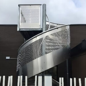 Escalier hélicoïdal en métal avec garde-corps perforé fixé à une façade de bâtiment.