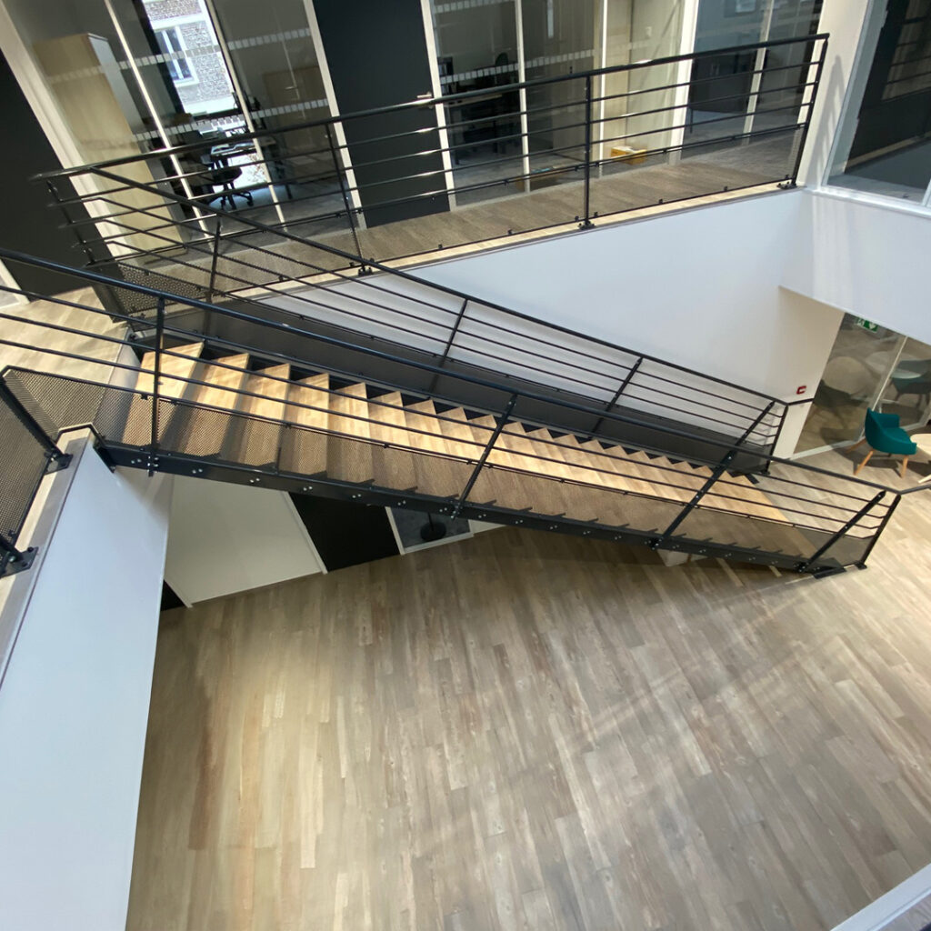 Escalier moderne en bois et acier avec garde-corps à lisses horizontales dans un hall lumineux.