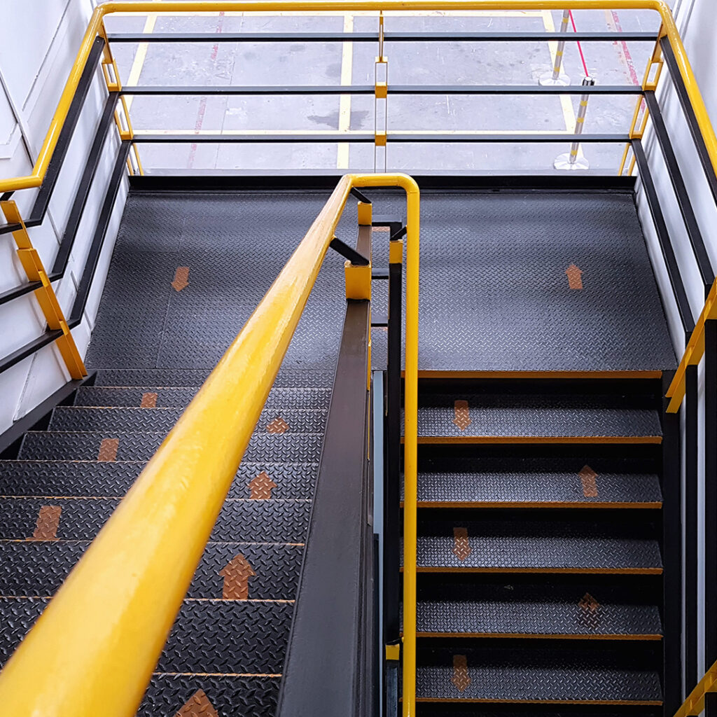 Escalier industriel en métal avec marches antidérapantes et main courante jaune de sécurité.