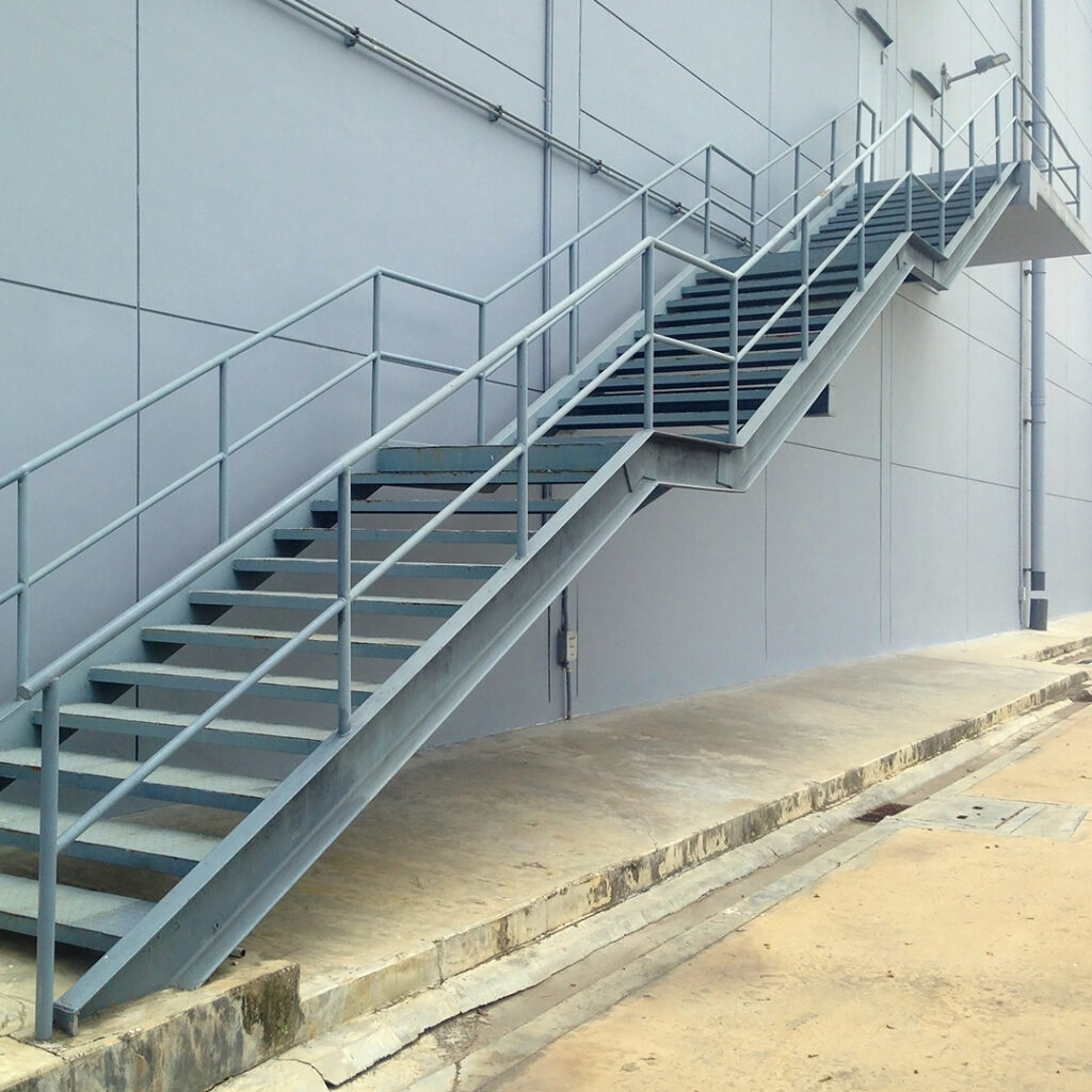 Escalier métallique extérieur fixé à une façade, avec garde-corps tubulaire.