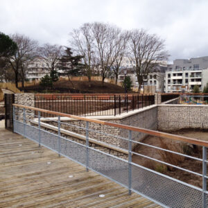 Passerelle en bois avec garde-corps métalliques surplombant un aménagement paysager urbain.