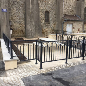 Garde-corps en acier noir délimitant un espace pique-nique près d’un bâtiment en pierre.