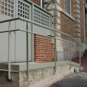 Rampe d’accès PMR avec main courante métallique devant un bâtiment en brique.