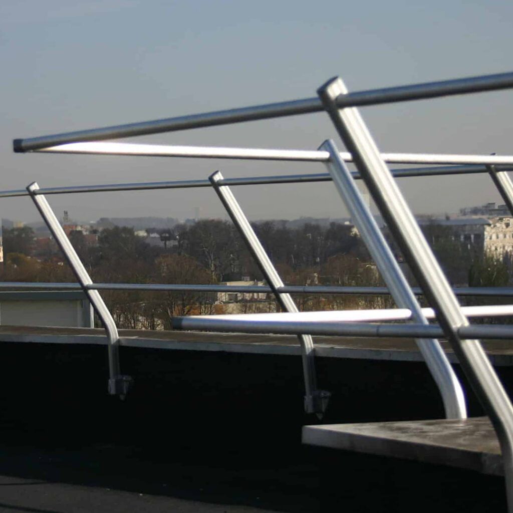 Garde-corps en acier galvanisé incliné, fixé sur acrotère pour sécuriser l’accès en toiture technique d’un bâtiment.