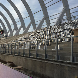 Garde-corps métallique installé devant des gradins dans une tribune de stade couvert.