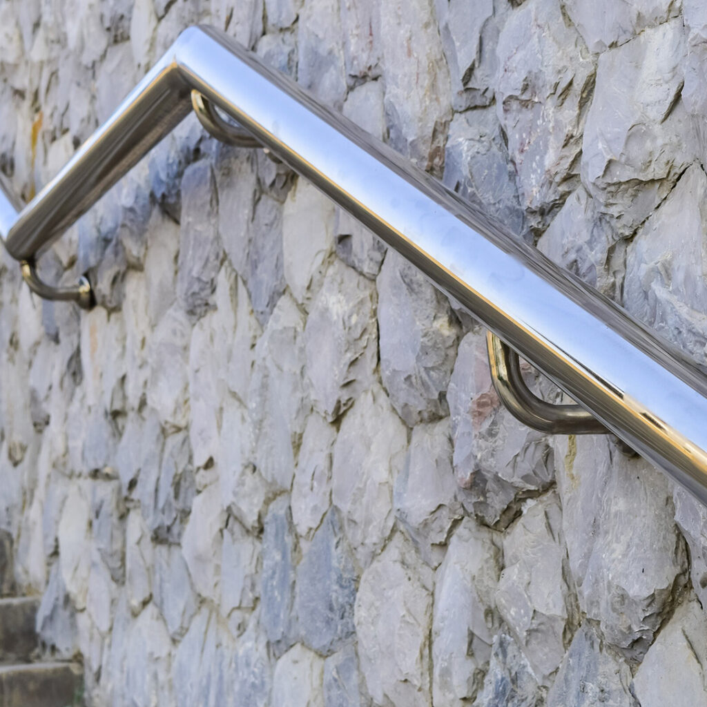 Main courante en inox fixée sur un mur en pierre naturelle, installée pour sécuriser une volée de marches en extérieur.