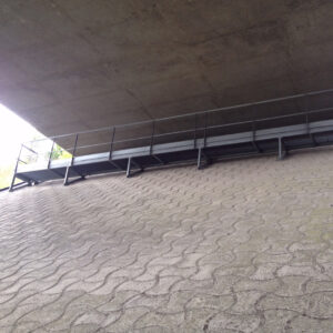 Passerelle technique métallique d’inspection installée sous un pont autoroutier.