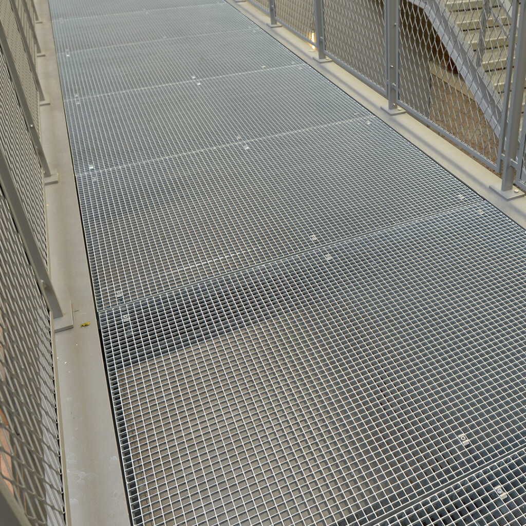 Passerelle en caillebotis métallique avec garde-corps en treillis déployé.
