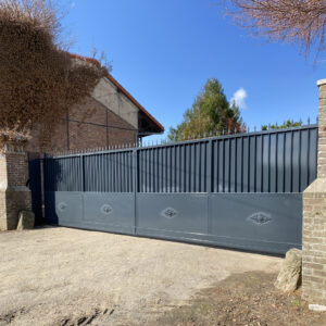 Portail coulissant en métal gris anthracite avec soubassement décoratif, installé entre deux piliers en briques.