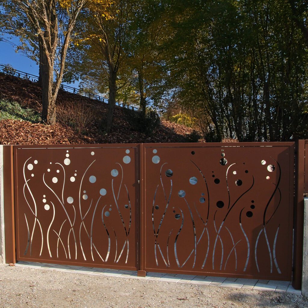 Portail en acier corten ajouré au motif végétal devant une allée arborée.