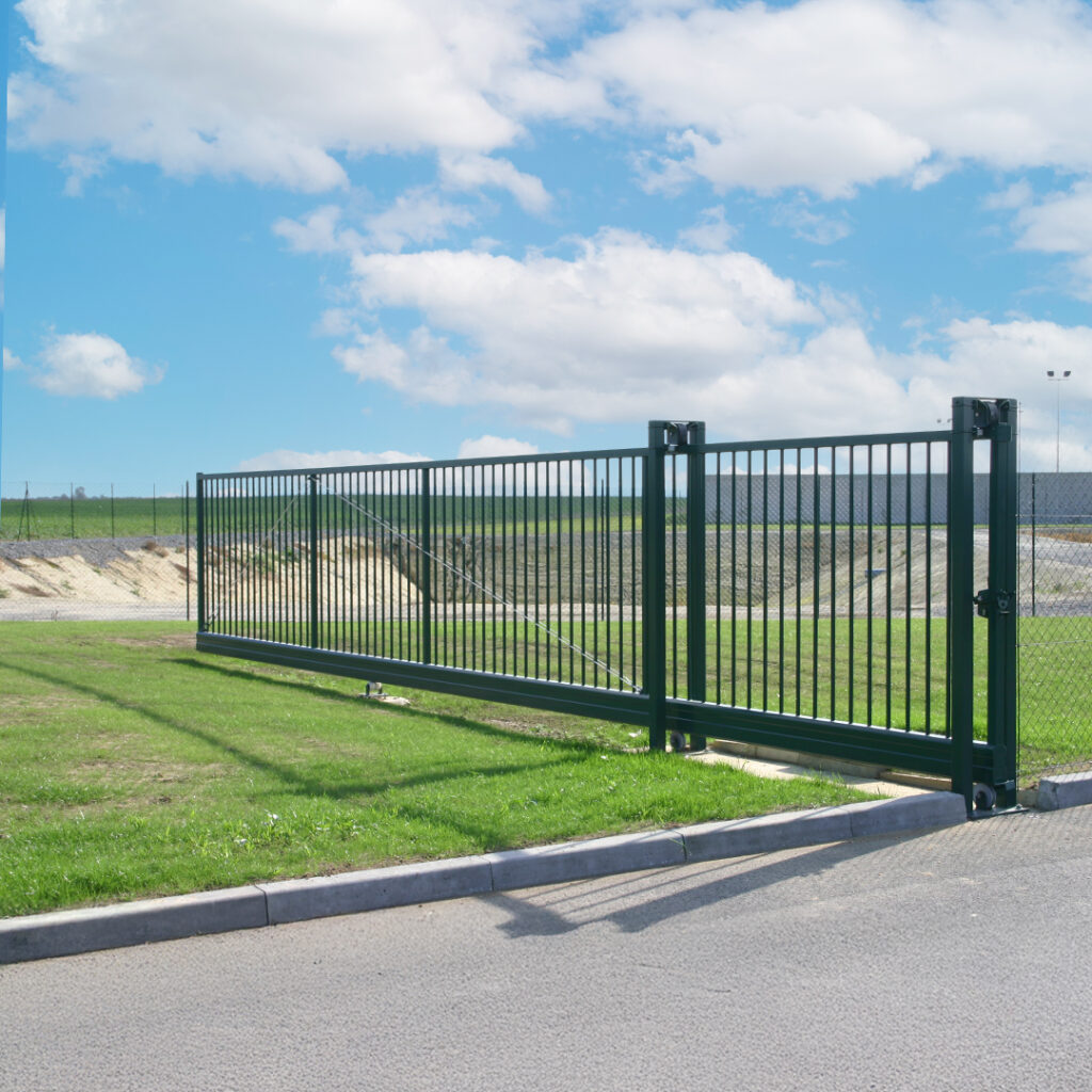 Portail coulissant industriel en acier avec barreaux verticaux, installé sur un site logistique.
