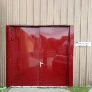 Porte métallique rouge à double battant sur bâtiment industriel.