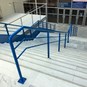 Rampes métalliques bleues sur escaliers en marbre blanc à l'entrée d'un complexe aquatique.