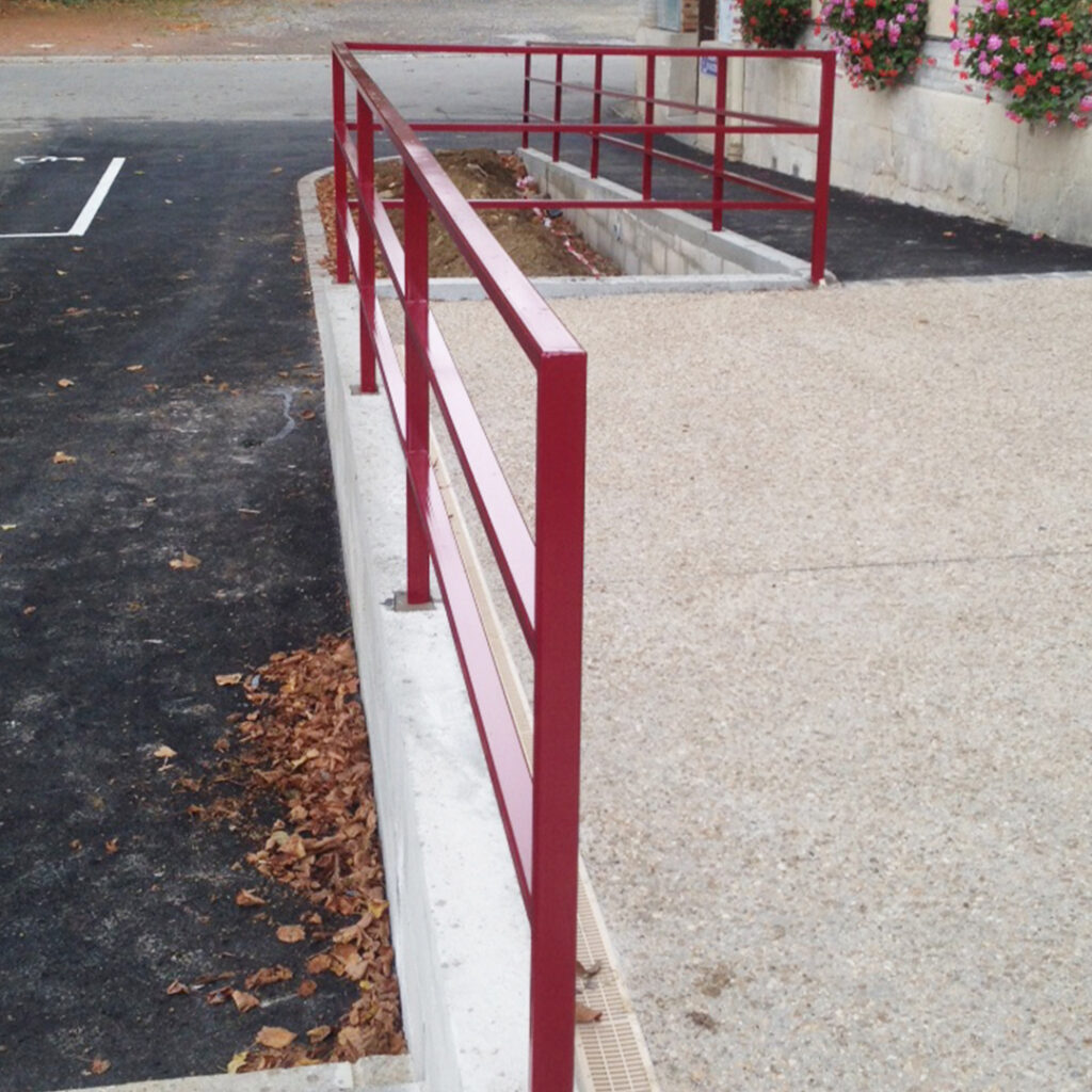 Rampe d’accès PMR avec garde-corps en acier rouge thermolaqué, installée devant un bâtiment public pour assurer l’accessibilité aux personnes à mobilité réduite.