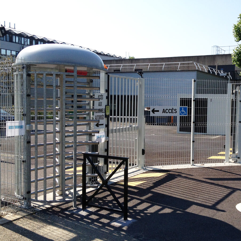 Zone d’accès sécurisé équipée d’un tourniquet pleine hauteur, d’un portillon PMR et d’un portail, installés sur un site tertiaire ou industriel.